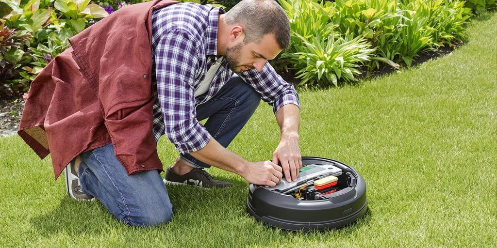 En person inspekterar en trasig robotgräsklippare i trädgården.